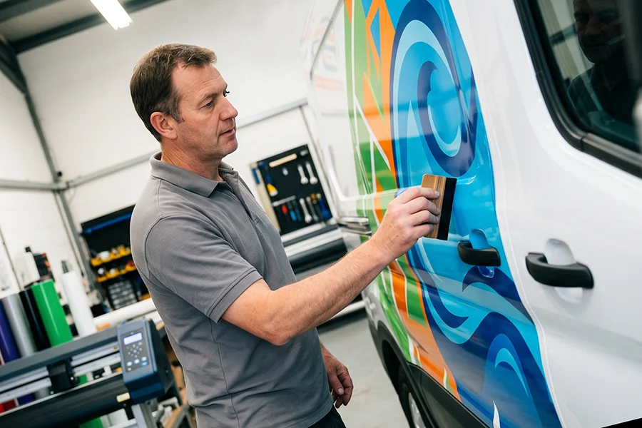 A man in a graphics shop applying a vehicle wrap to a van
